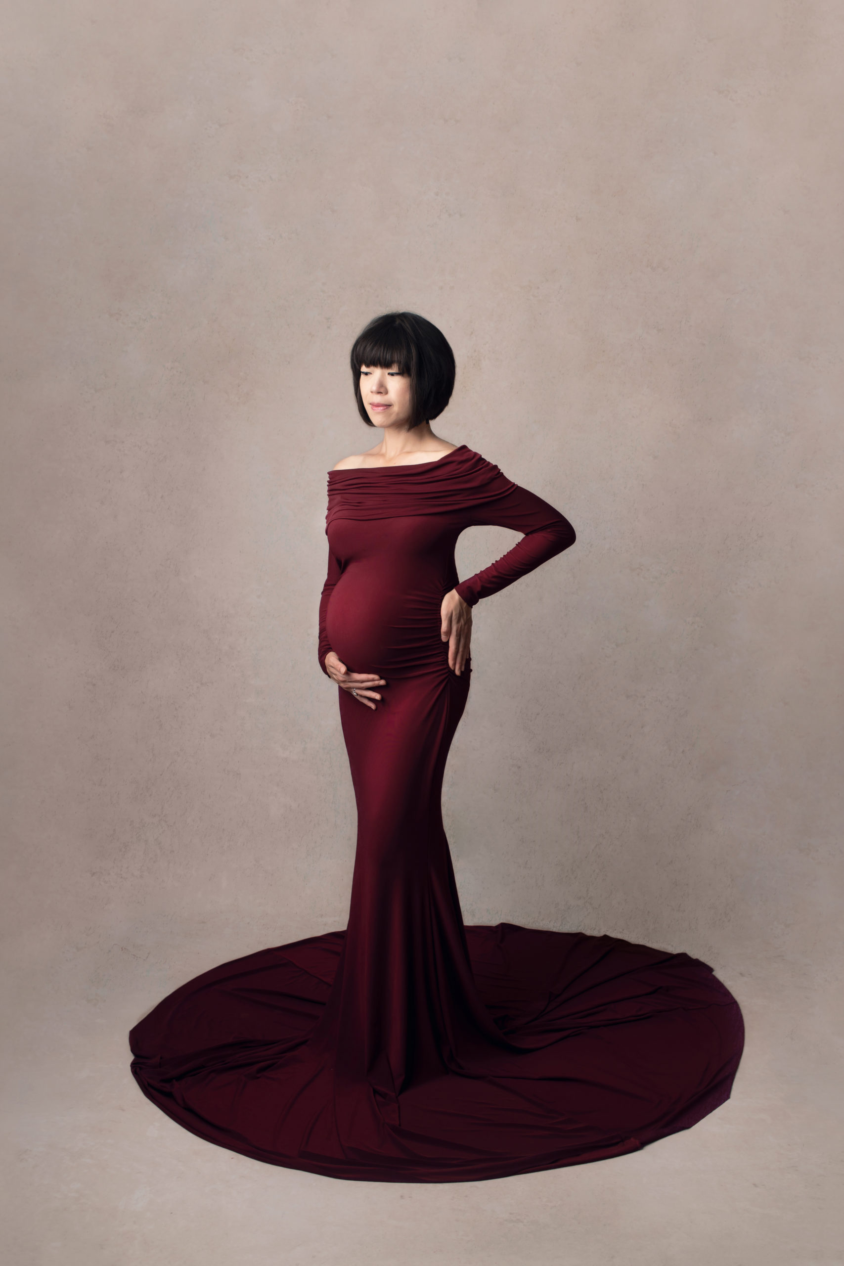 Photo grossesse de belle femme enceinte Asiatique dans la robe rouge avec le fond de studio beige réalisée pendent une séance grossesse stylisée avec maquillage et coiffure professionnelles