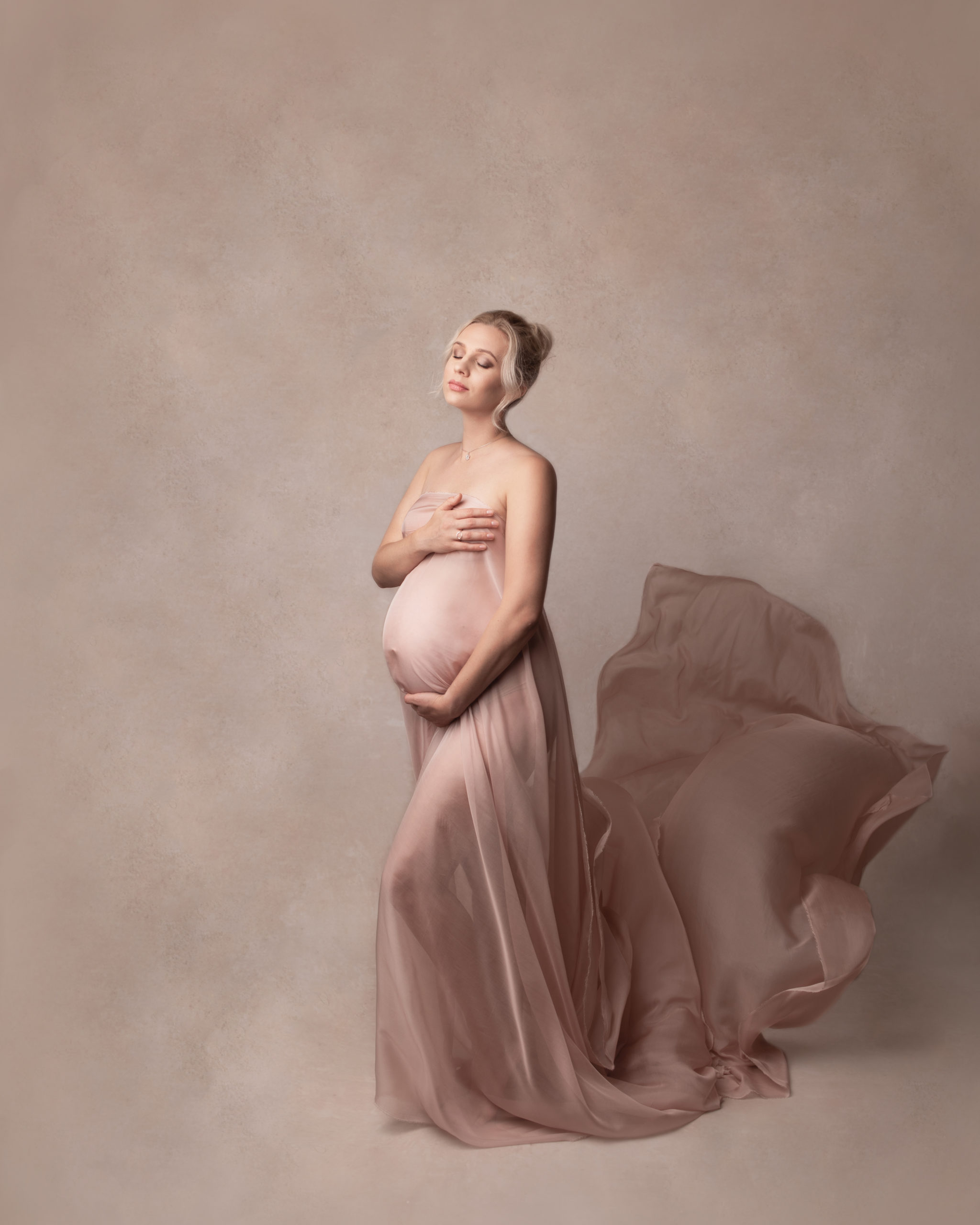 Photo grossesse de belle femme enceinte avec la soie volante Italien rose avec le fond de studio beige réalisée pendent une séance grossesse stylisée avec maquillage et coiffure professionnelles